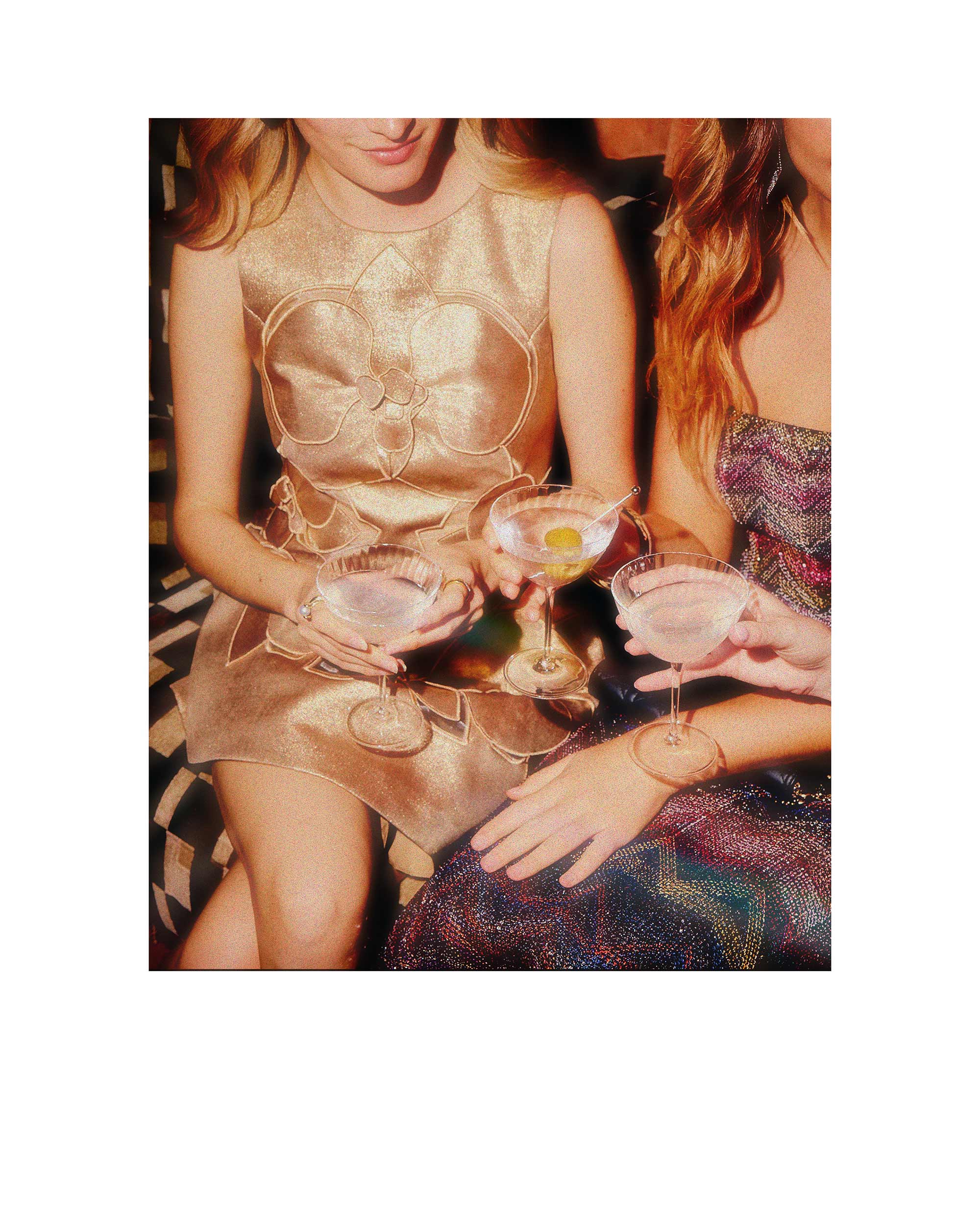 Two women in evening gowns holding cocktails in a close-up shot.